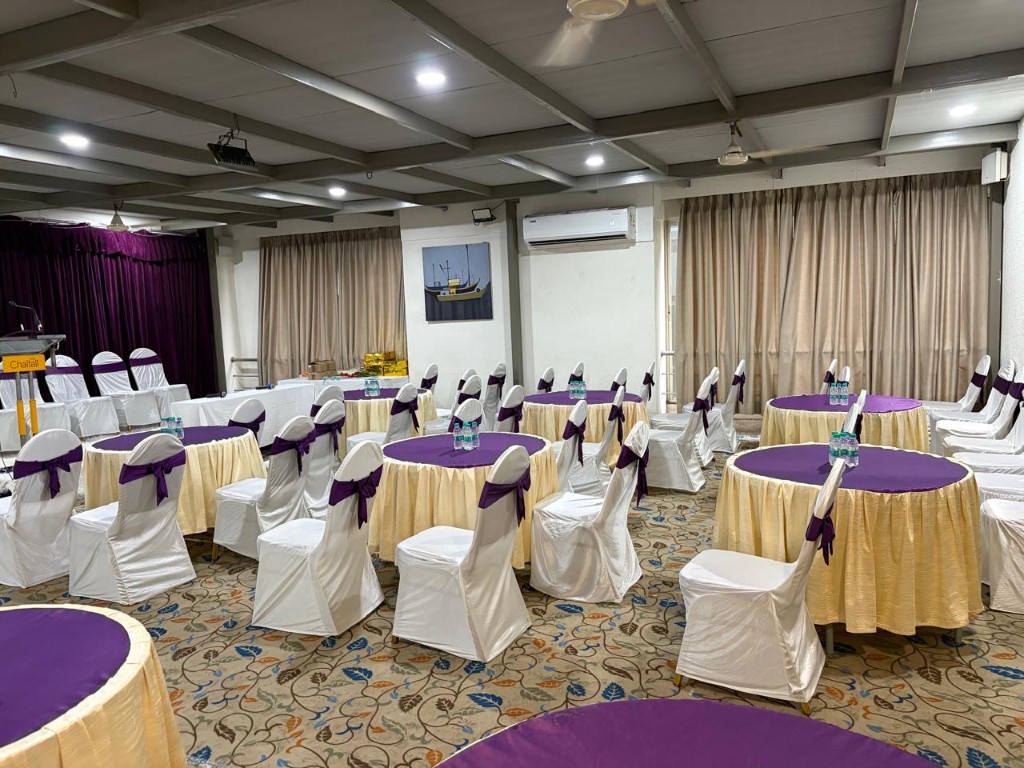 Banquet hall at Hotel Chaitali with round tables, white chairs and purple sashes
