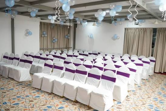 Banquet hall seating with white chair covers and purple sashes at Hotel Chaitali
